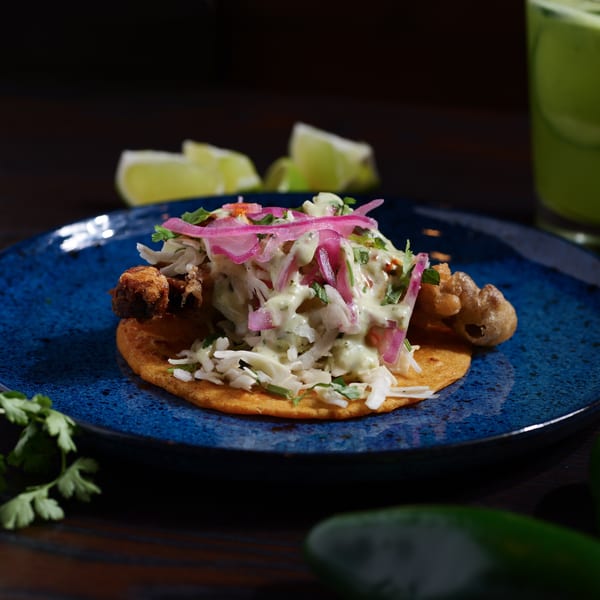 A Str8 up Tacos fried fish taco with cabbage, pickled onions, and crema on a blue plate.