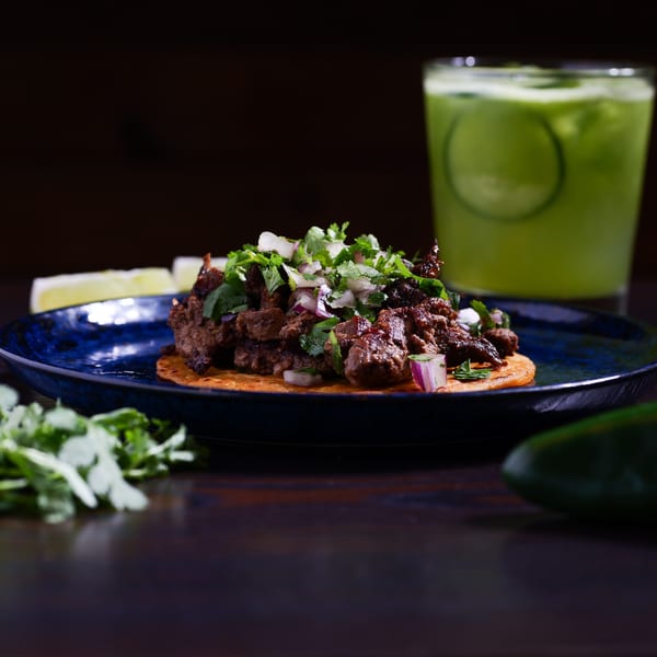 A Str8 up Tacos carne asada taco with cilantro and onions, next to a green drink.