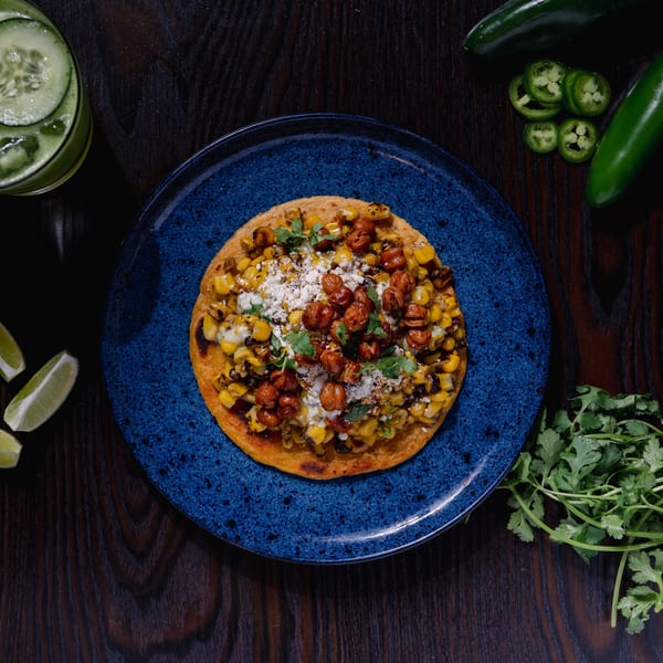 Str8 up Tacos' tostada with corn, chickpeas, cheese, and cilantro, surrounded by limes and jalapeños.