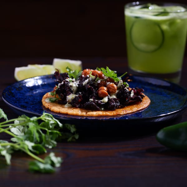 A Str8 up Tacos' dark mushroom taco with chickpeas, cilantro, and sauce, next to a green drink.