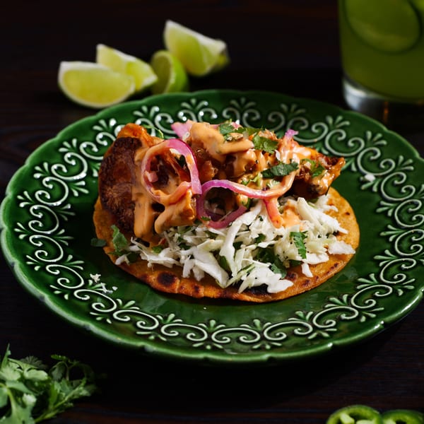 A Str8 up Tacos fried fish taco with cabbage, red onions, and sauce on a green plate.