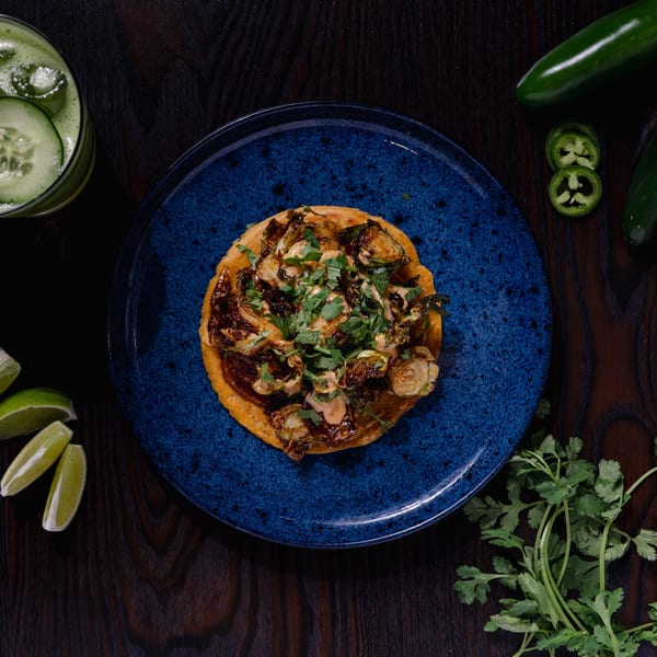 A Str8 up Tacos tostada with roasted Brussels sprouts, sauce, and cilantro on a blue plate.